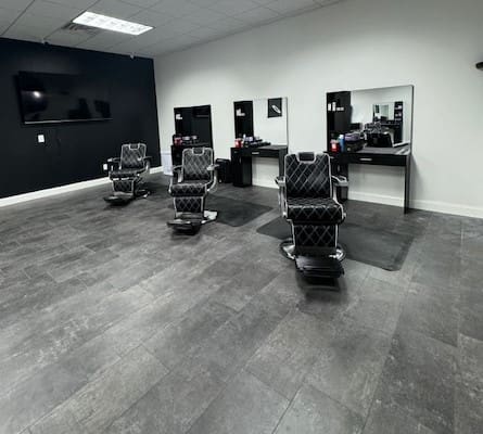 A barber shop with three black chairs and two mirrors.